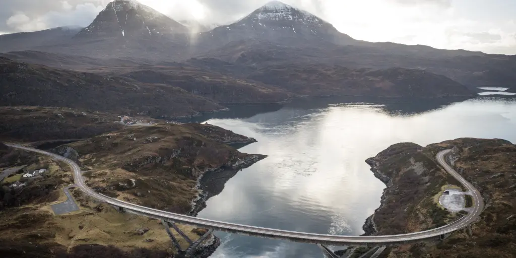 An aerial view of the curved Kylesku Bridge, Scotland, with two munros in the background