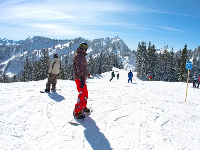 Snowboarders and skiers getting ready to go down a slop in the ski resort
