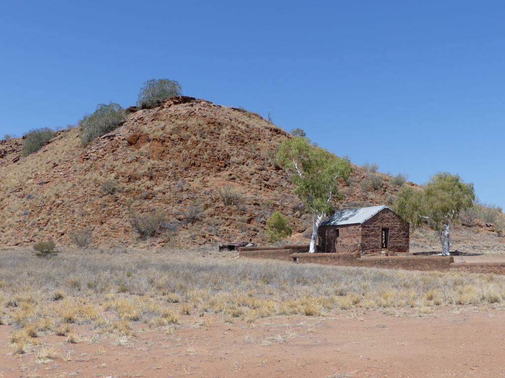 Lonely, old sandstone brick house between two white ghost gum trees by a hill at the old Barrow Creek Telegraph Station in Northern Territory, Australia