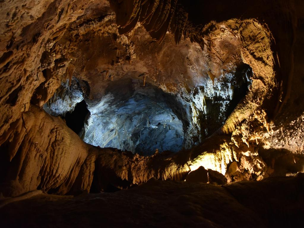 The inside of a cave at Shasta Lake, with stalactites, stalagmites and lime deposits, plus a glimmer of light streaming through