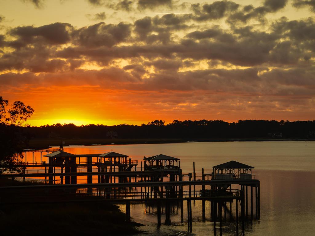 Wooden piers silhouetted by the riverbank, with bright orange sunset light coming over the horizon