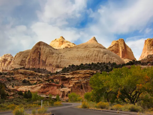 A road winding towards majestic scenery of peaky sand-colored domes in Capitol Reef National Park on a partially cloudy day