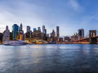 Outdoors view on NYC New York City Brooklyn Bridge Park by east river, cityscape skyline at sunset, dusk, twilight, blue hour, dark night, skyscrapers, buildings, waves, tour boat