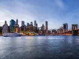 Outdoors view on NYC New York City Brooklyn Bridge Park by east river, cityscape skyline at sunset, dusk, twilight, blue hour, dark night, skyscrapers, buildings, waves, tour boat