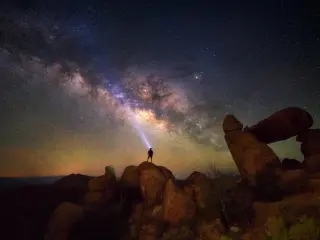 Night time view of star constellation and galaxy at Balanced Rock, Big Bend National Park, with silhouetted profile of someone standing on the rockface