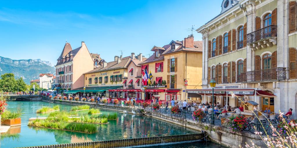 Restaurants and cafes alongside a turquoise canal on a sunny day in Annecy, France