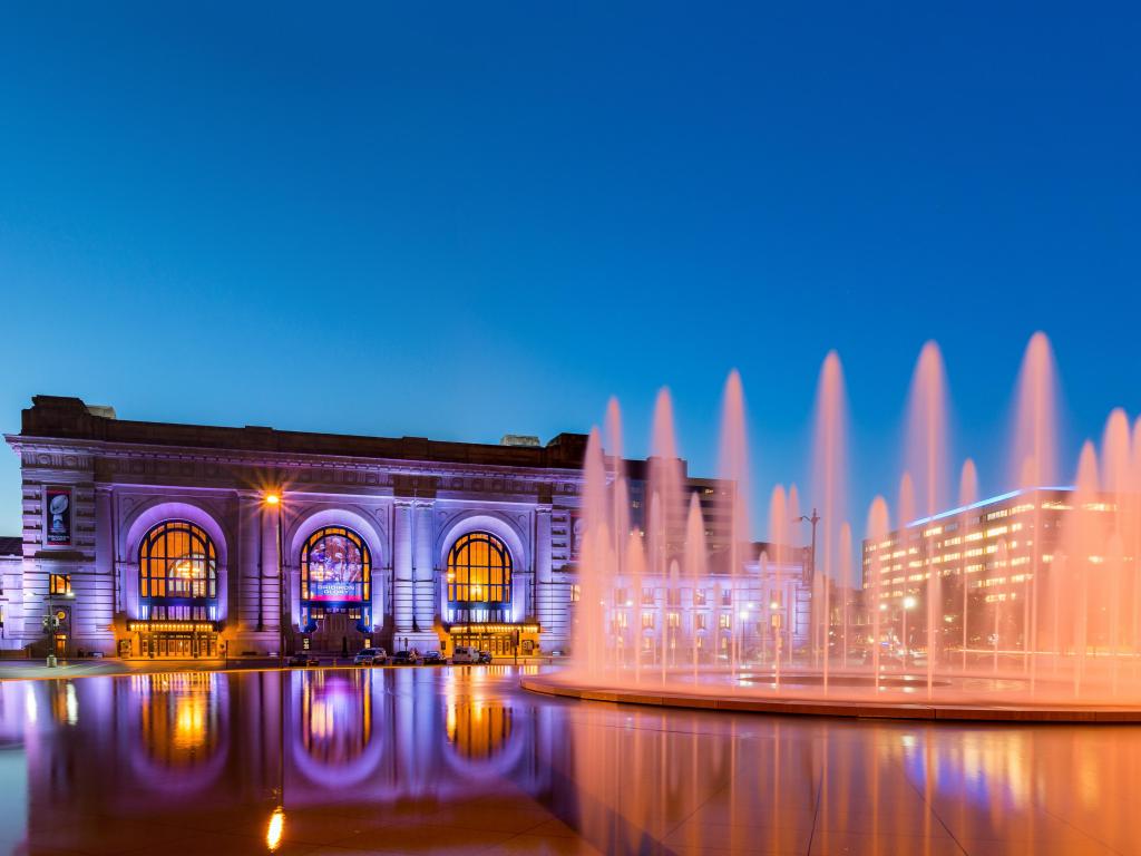 Illuminated station building and lake with fountain at sunset