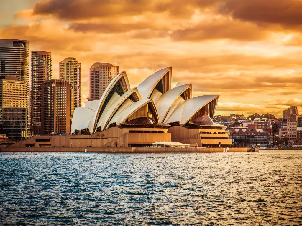Sail-shaped outline of Sydney Opera House viewed from a ferry travelling across the harbour, lit up in golden light