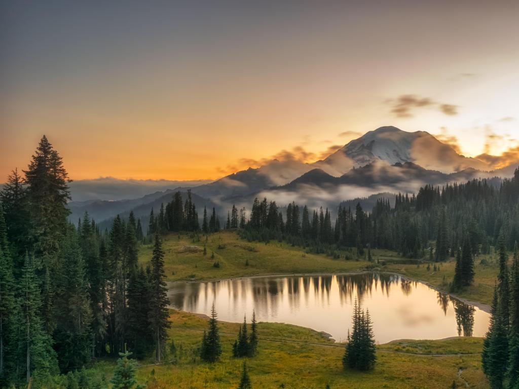 Mount Rainier National Park, Washington at sunrise with a lake and forest in the foreground and mountains covered with fog in the background.