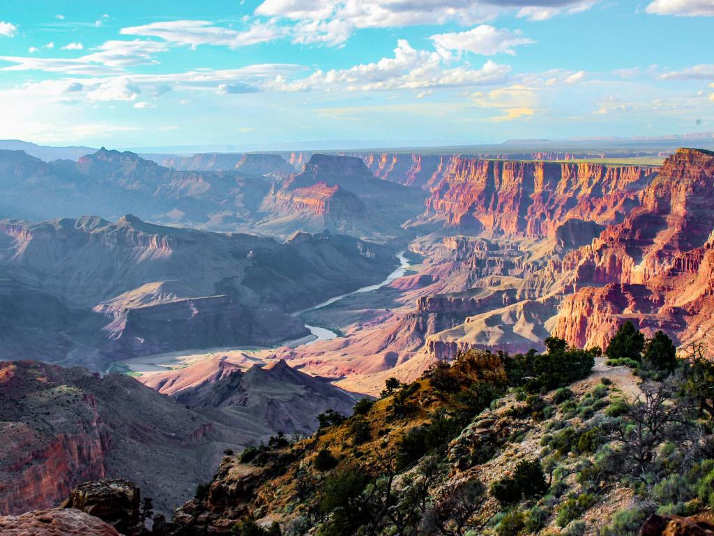 Grand Canyon on a mostly clear day with only a few clouds and blue skies. The photo depicts the famous red rock formations of the canyon with a valley below.