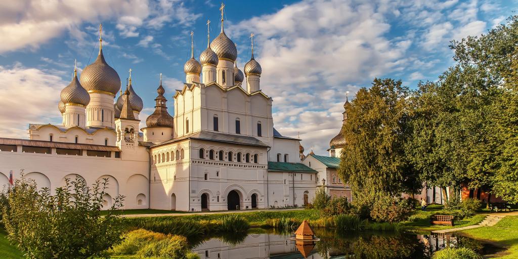 A view of the Rostov Veliky Kremlin with its silver domes and a garden in front of it, at golden hour