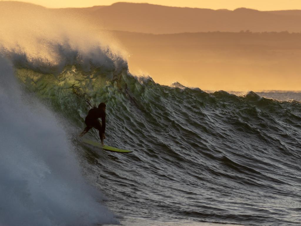 The silhouette of a surfer at sunrise riding a wave at Jeffreys Bay in South Africa