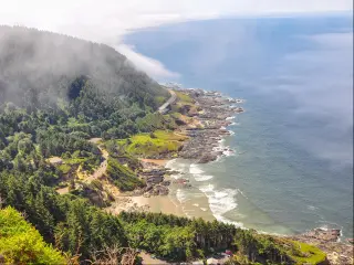 Cape Perpetua, Oregon with fog rolling over the tree-lined mountains, a calm sea and a quiet beach. 