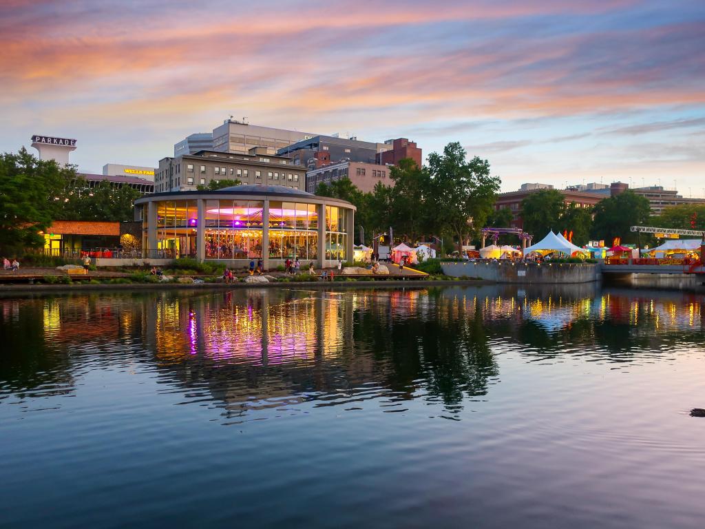 Spokane, Washington, USA taken at the Looff Carousel which is colorfully illuminated and reflects in the river alongside festival food tents and shops at sunset during Pig Out in the Park Festival.