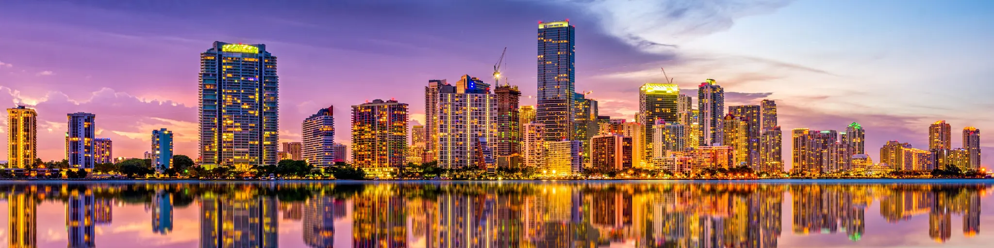 Colorful lit-up skyline of the city reflected on the water during a pink and purple sunset