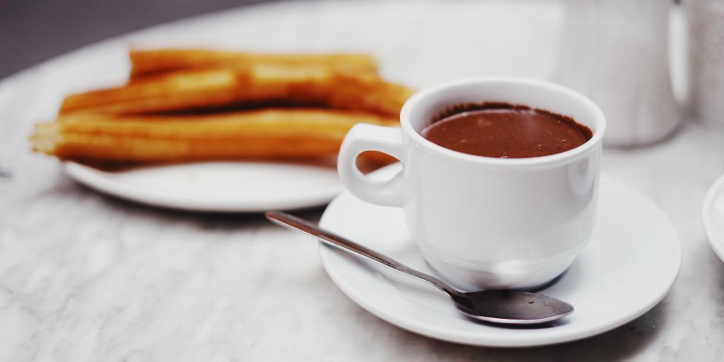 A cup of hot dipping chocolate on a table next to a plate of churros