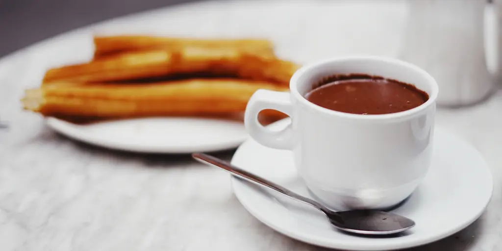 A cup of hot dipping chocolate on a table next to a plate of churros