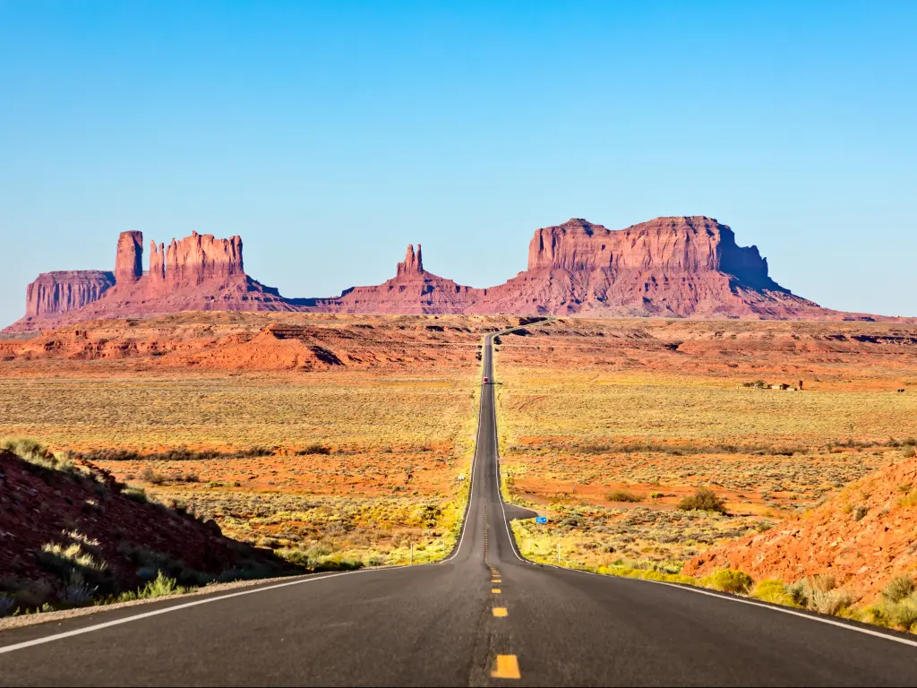 Monument Valley, USA with a scenic road leading to Monument Valley against a blue sky.