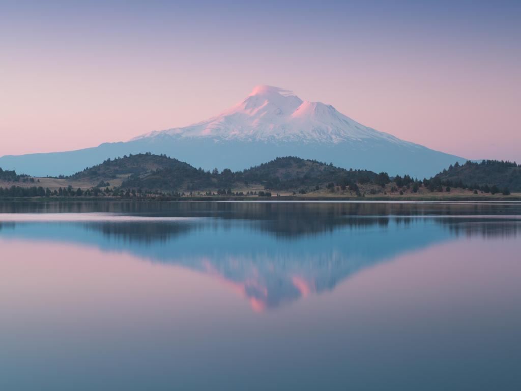 Snow capped mountain reflected in clear lake at sunrise