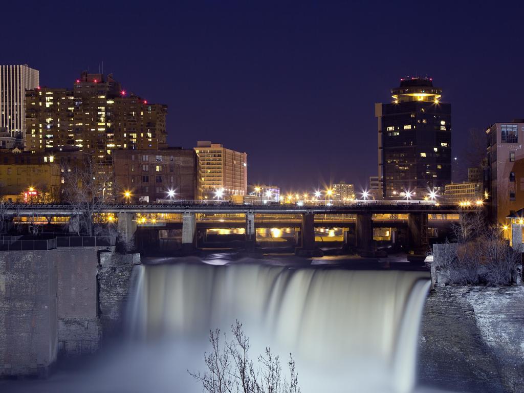 Rochester, New York, USA with the night skyline of the city skyscrapers in the background and the waterfall in the foreground.