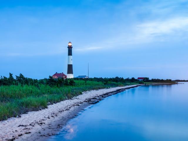 An image of the famous landmark in Fire Island, the Lighthouse. The sea, green grasses and the blue sky is on the picture.