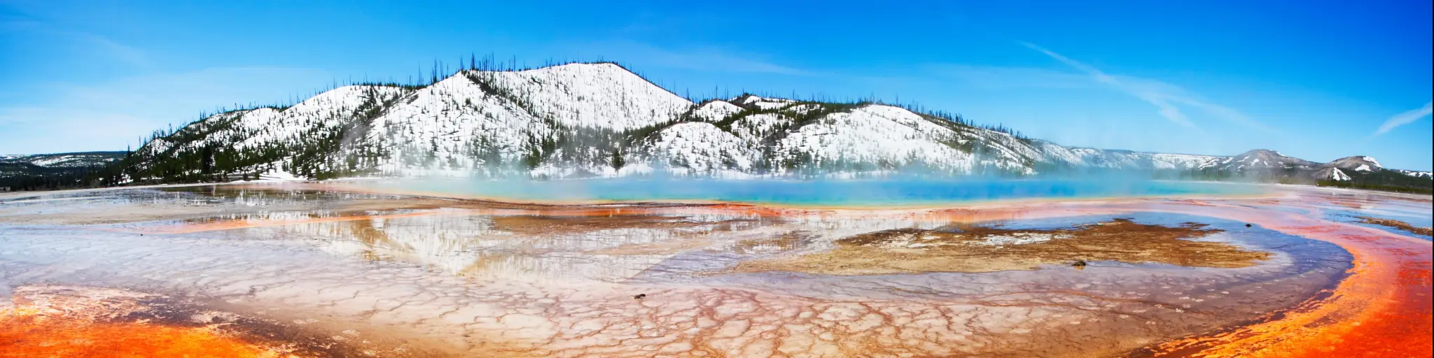 Vibrant colors of the Midway Geyser Basin at Yellowstone National Park, with snowy mountains in the background
