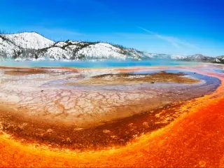 Vibrant colors of the Midway Geyser Basin at Yellowstone National Park, with snowy mountains in the background