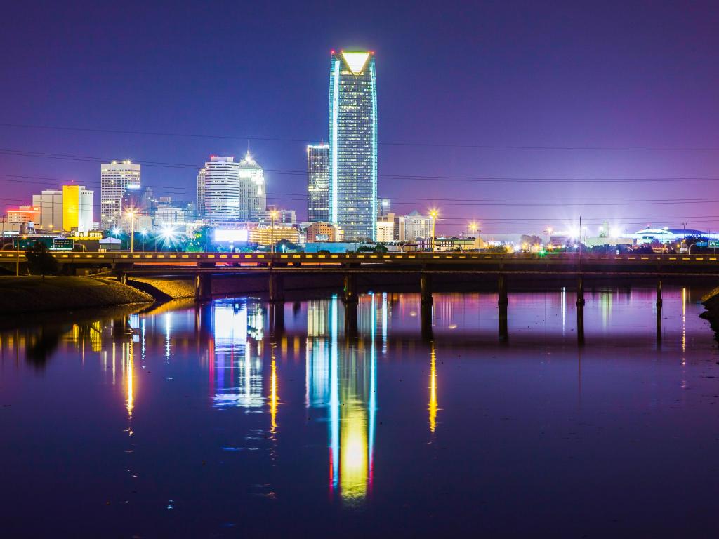 Oklahoma City skyline at night with the bridge in the foreground and skyline in the distance.