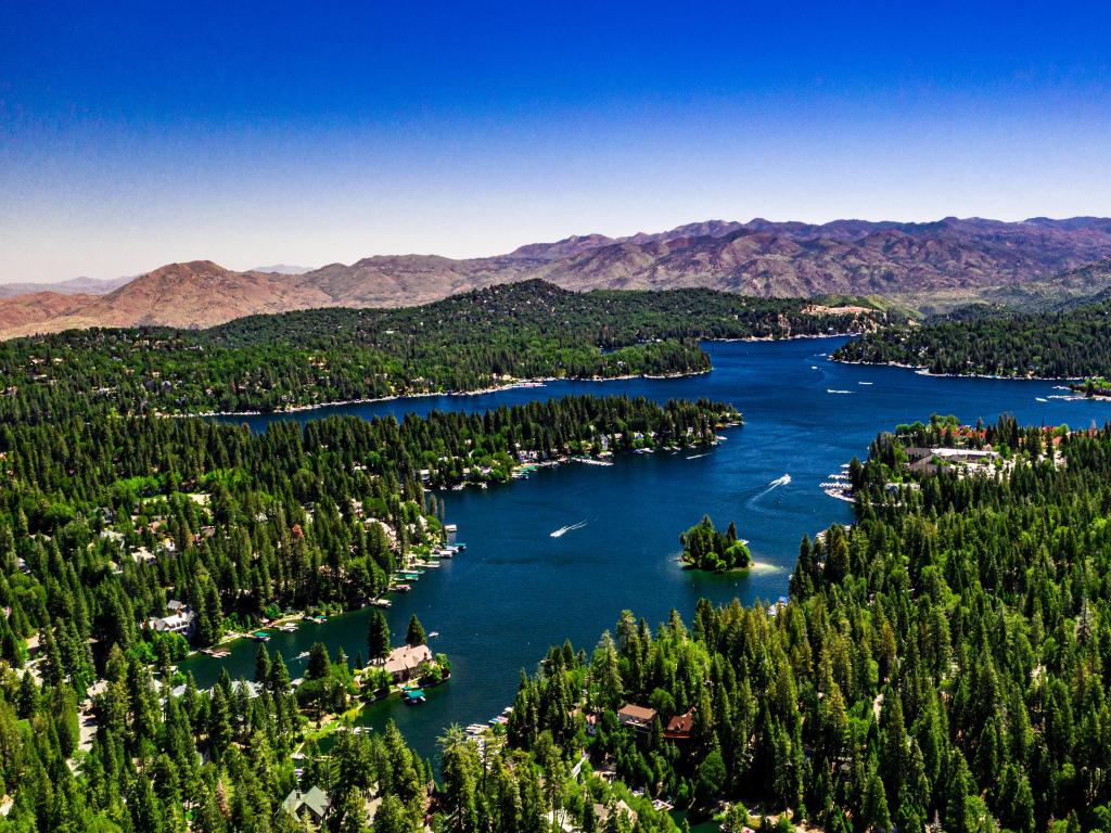 Lake Arrowhead, San Bernardino Mountains, California, USA taken as an aerial drone panorama of the lake on a clear, summer day with blue water and sky, purple mountains and green trees.