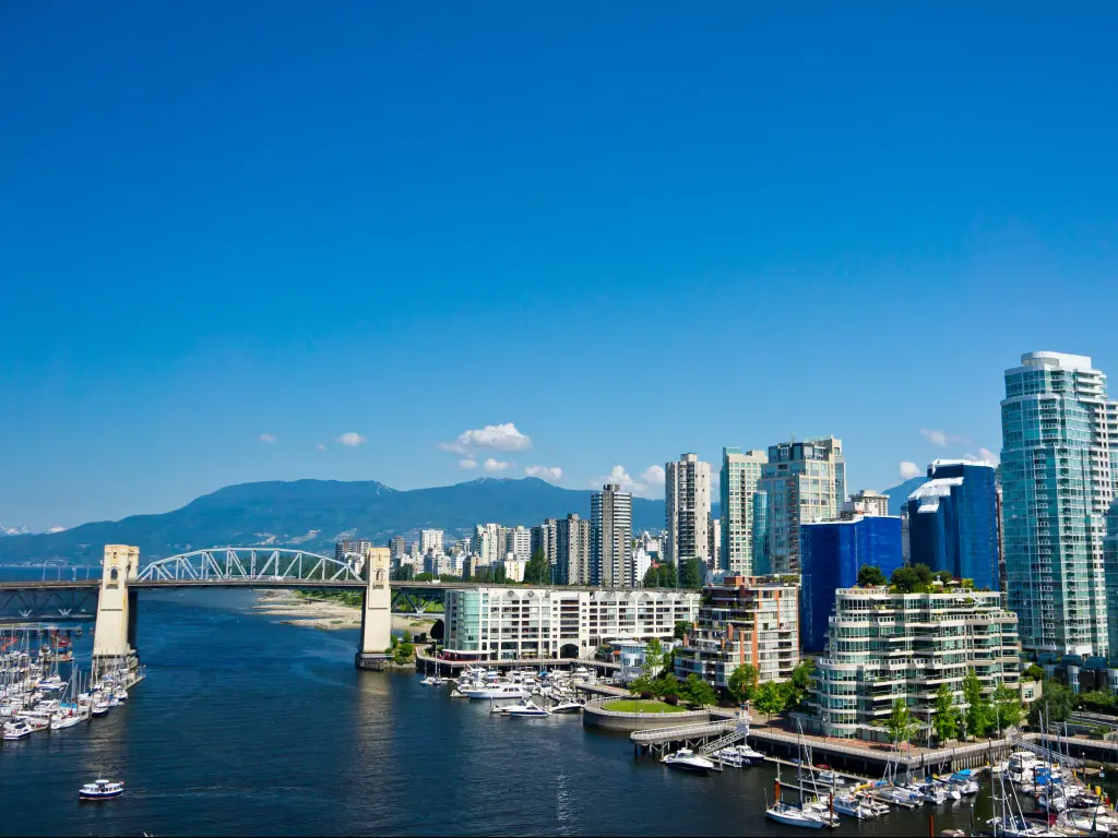 Vancouver, British Columbia, Canada with a beautiful view of the city in the background and the bridge crossing the water, plus mountains in the distance on a sunny clear day.