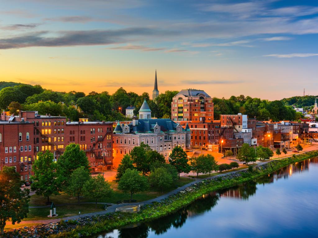 Augusta, Maine, USA downtown skyline on the Kennebec River taken at sunset with trees lining the river.