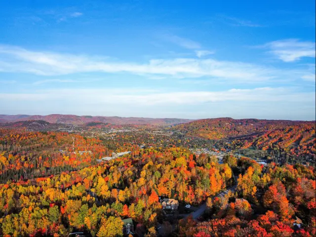 Aerial view of mid fall in Saint-Sauveur Quebec with orange and brown-hued trees and mountains in the background