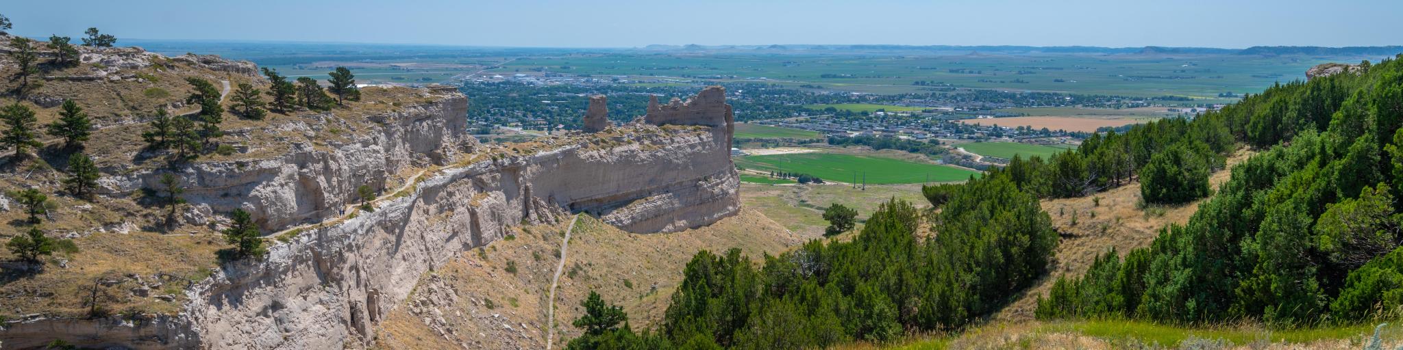 Panoramic view across Scotts Bluff National Monument and surrounding green and rugged landscape on clear day.
