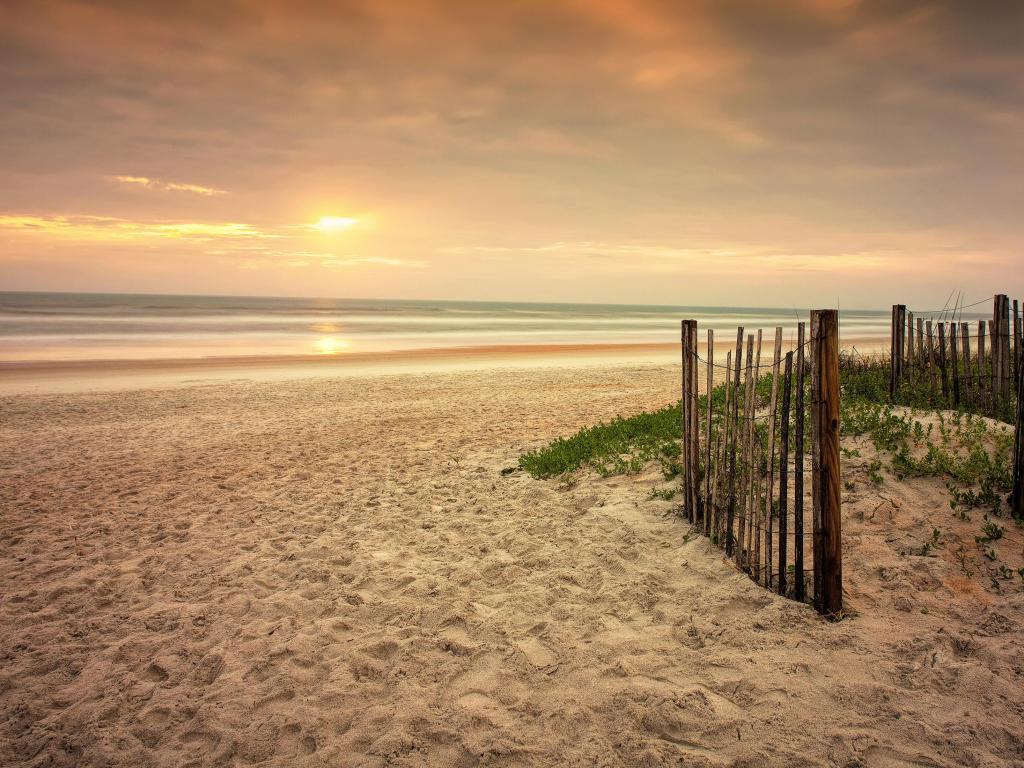 Ormond Beach, Florida, USA with a sandy beach, wooden fence and a distant sunset.