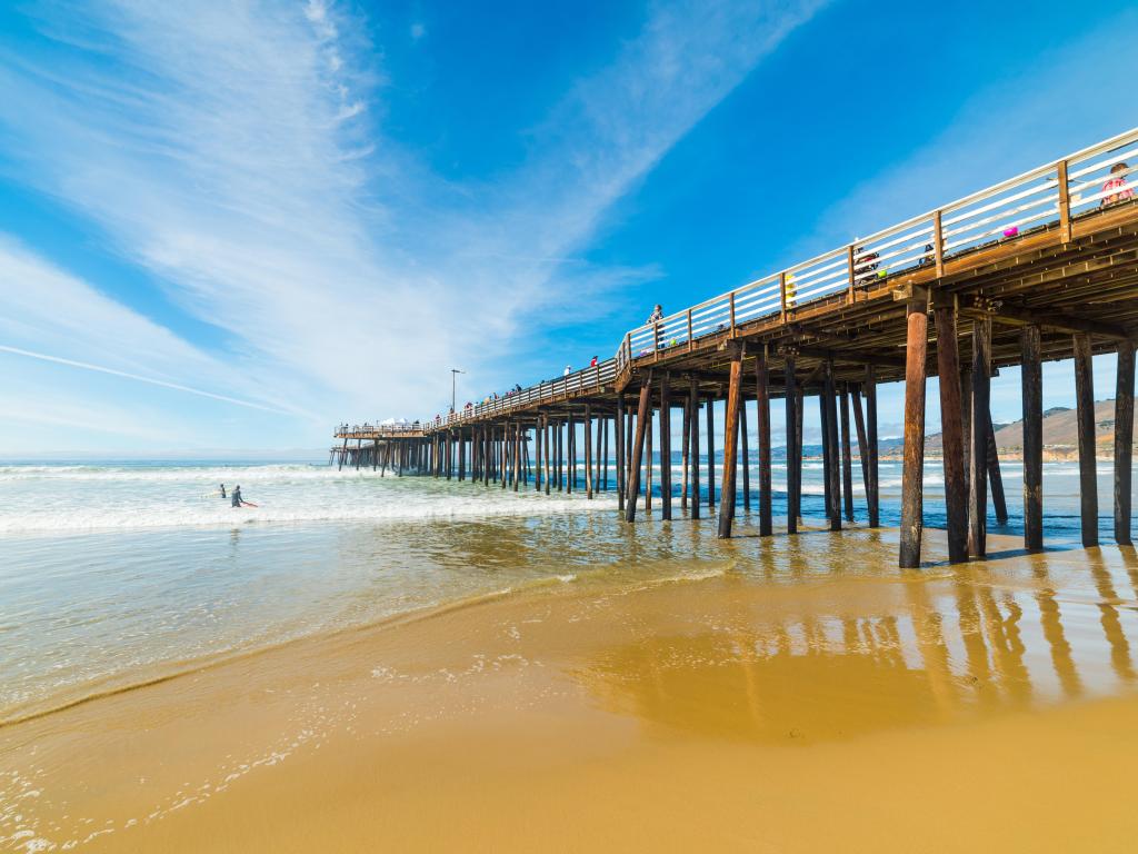 Surfers by Pismo Beach Pier in California on a sunny day. Photo is taken from the beach.