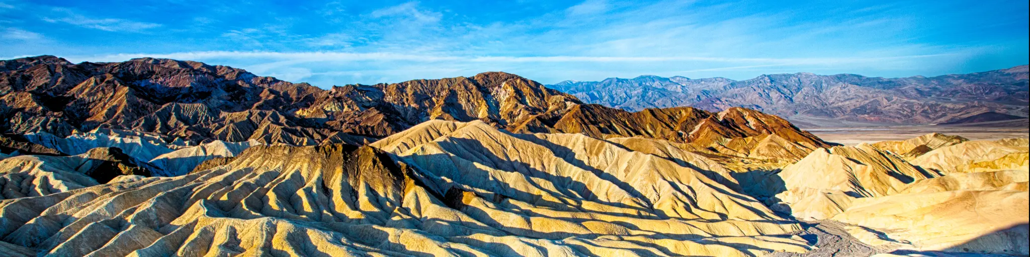 An image that shows how the Zabriskie Point in Death Valley National Park, California, USA looks during sunrise in a clear and bright sky. 