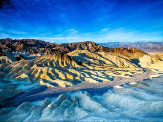 An image that shows how the Zabriskie Point in Death Valley National Park, California, USA looks during sunrise in a clear and bright sky. 