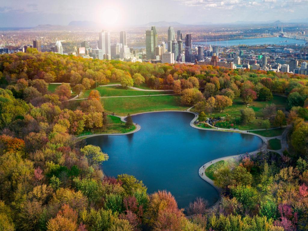 Montreal, Canada in Autumn with trees lining a large lake the middle and the city of Montreal in the background. 