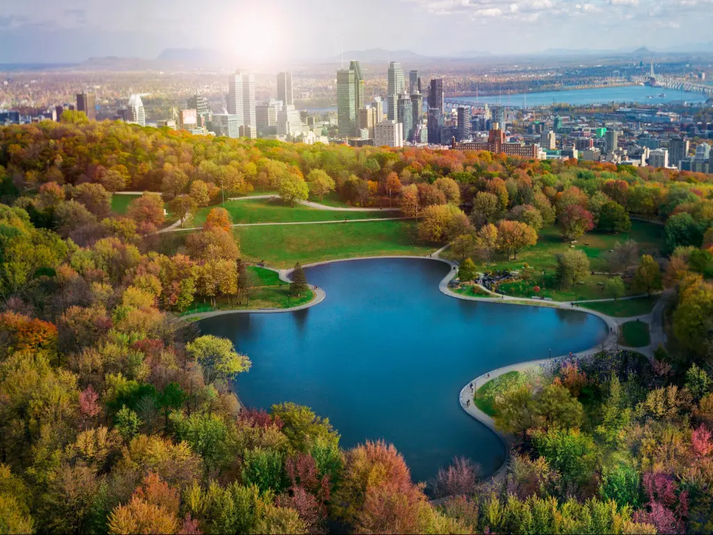 Montreal, Canada in Autumn with trees lining a large lake the middle and the city of Montreal in the background. 