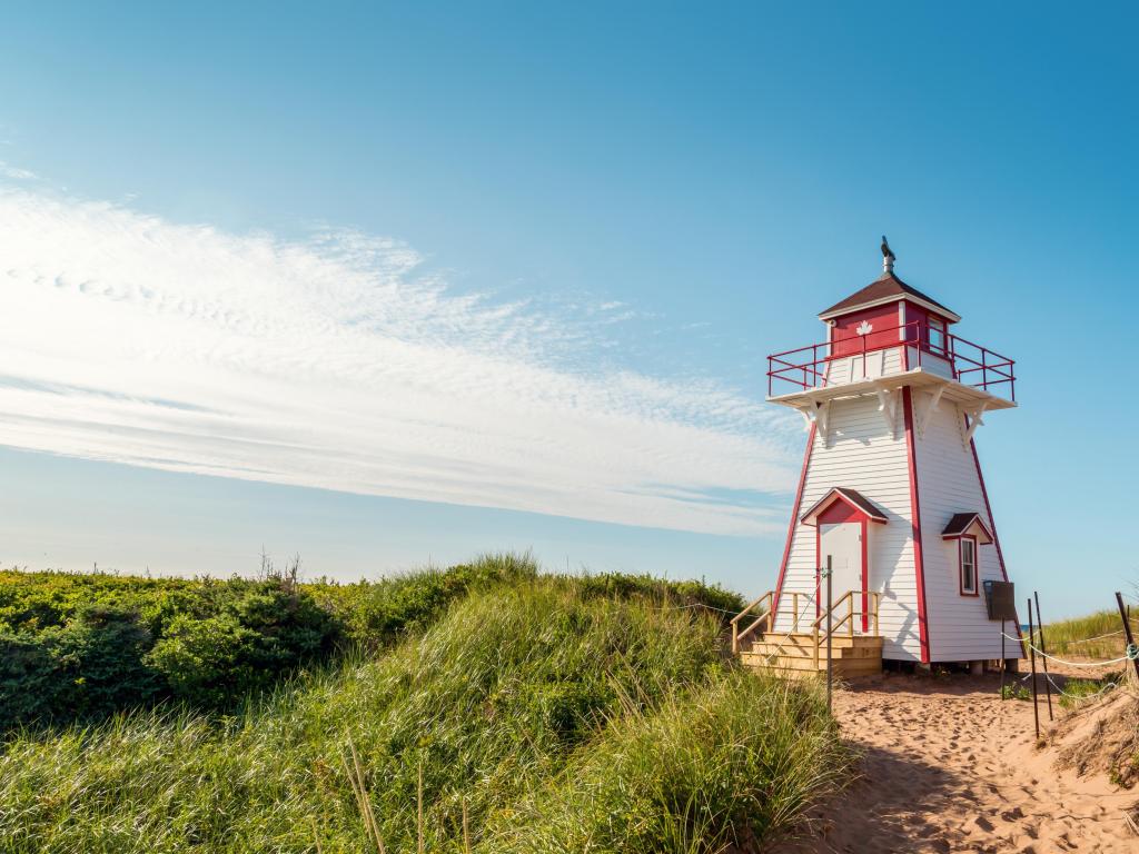 Covehead Lighthouse in Stanhope, Prince Edward Island, Canada with grass and sand in the foreground against a blue sky above.