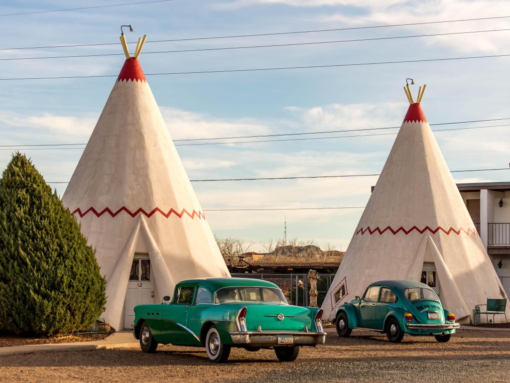 Two wigwams with blue colored vintage cars parked in the front