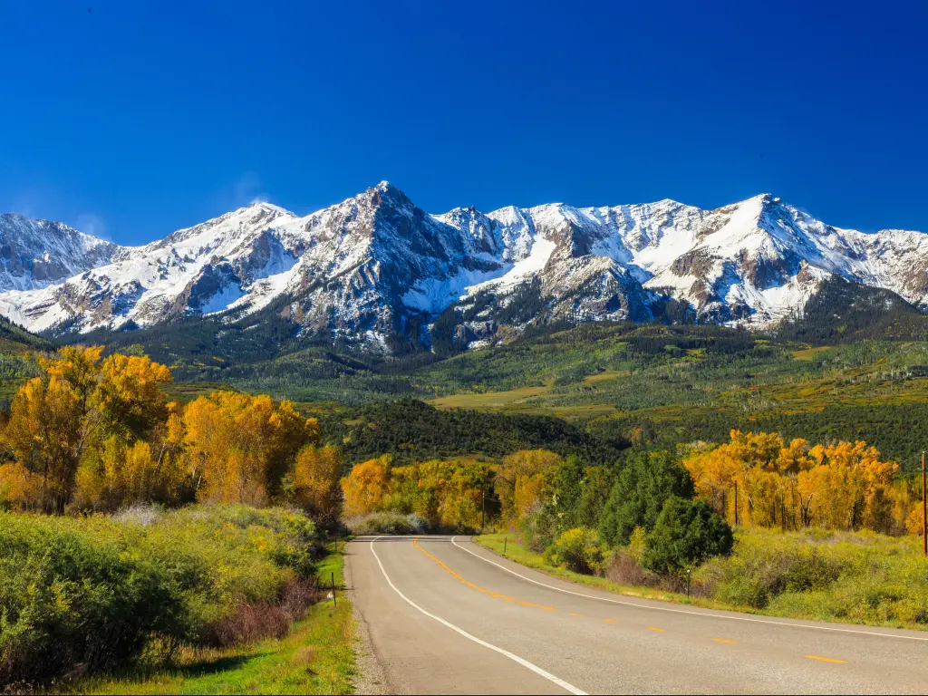 Countryside road with Rocky Mountains in the background, fall season in Colorado