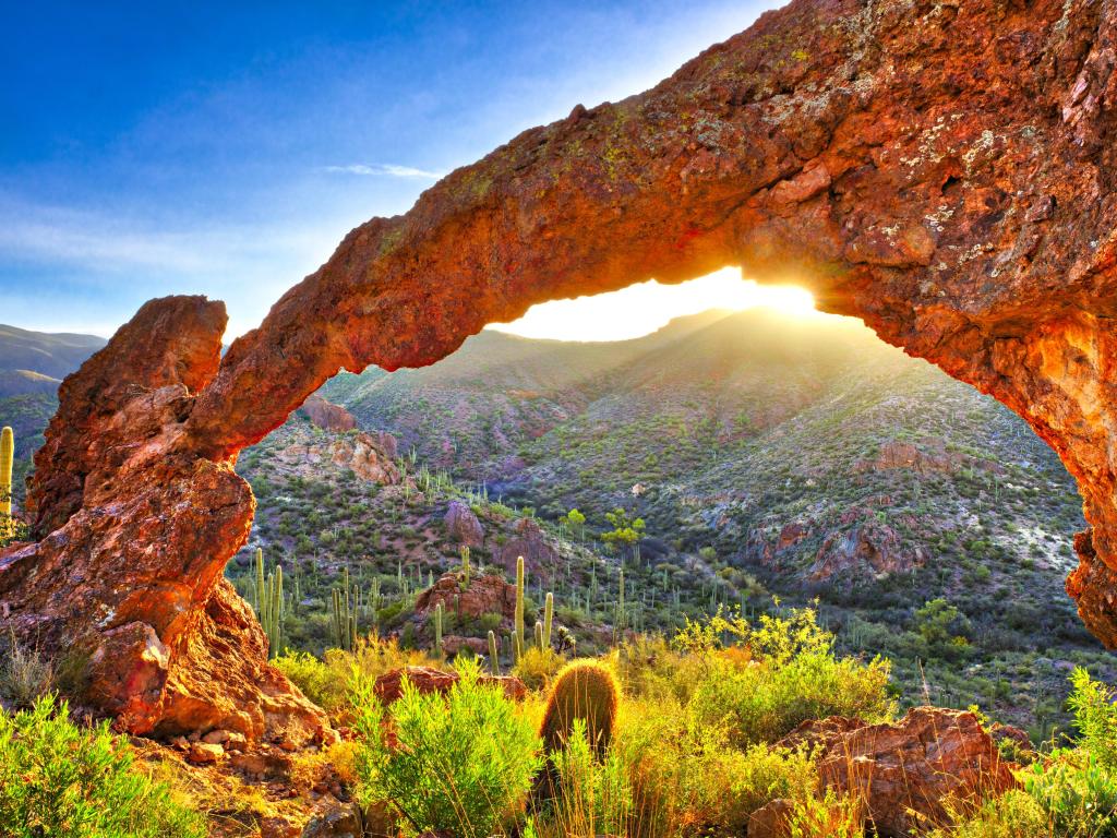View of desert through rocky arch with sunrise casting a bright ray of light
