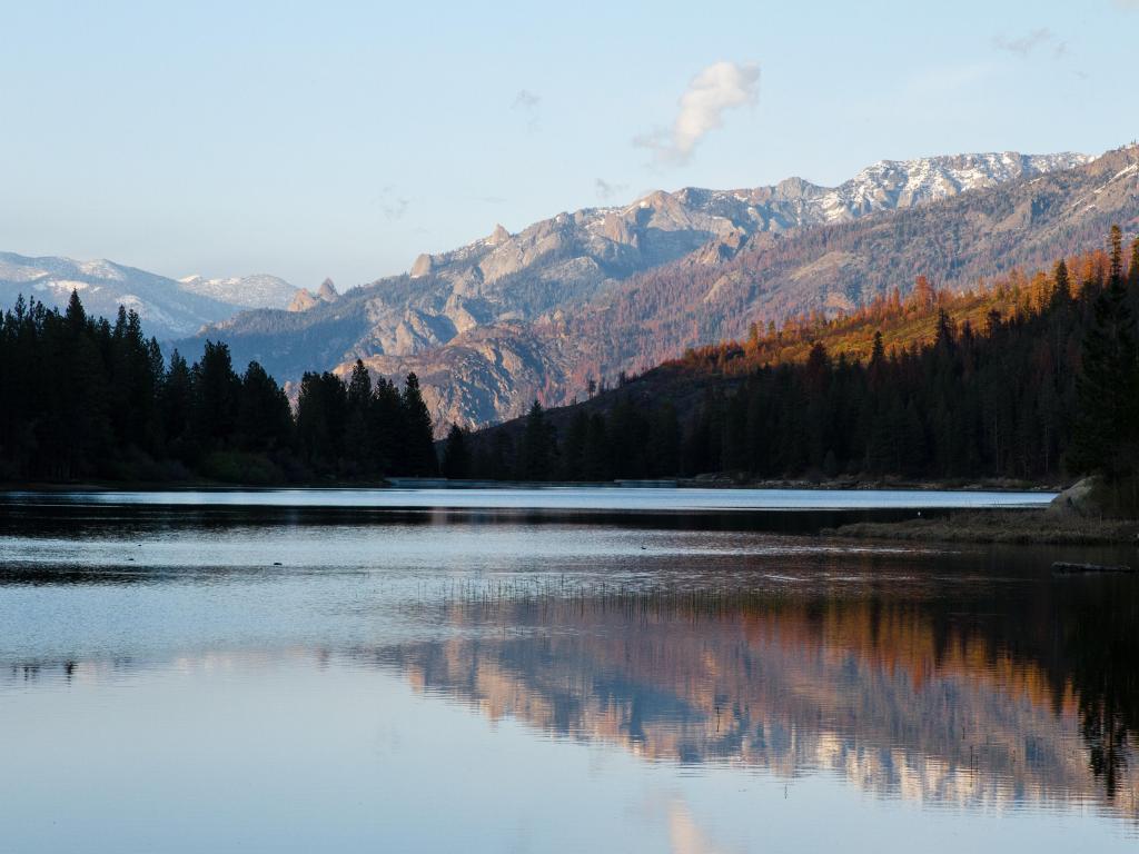 Kings Canyon National Park, USA with a vast lake in the foreground and mountains and trees in the distance reflecting in the water, taken on a clear sunny day.