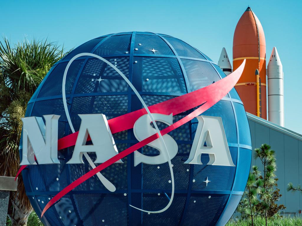 Blue NASA emblem at Kennedy Space Center, Florida, with an orange rocket in the background