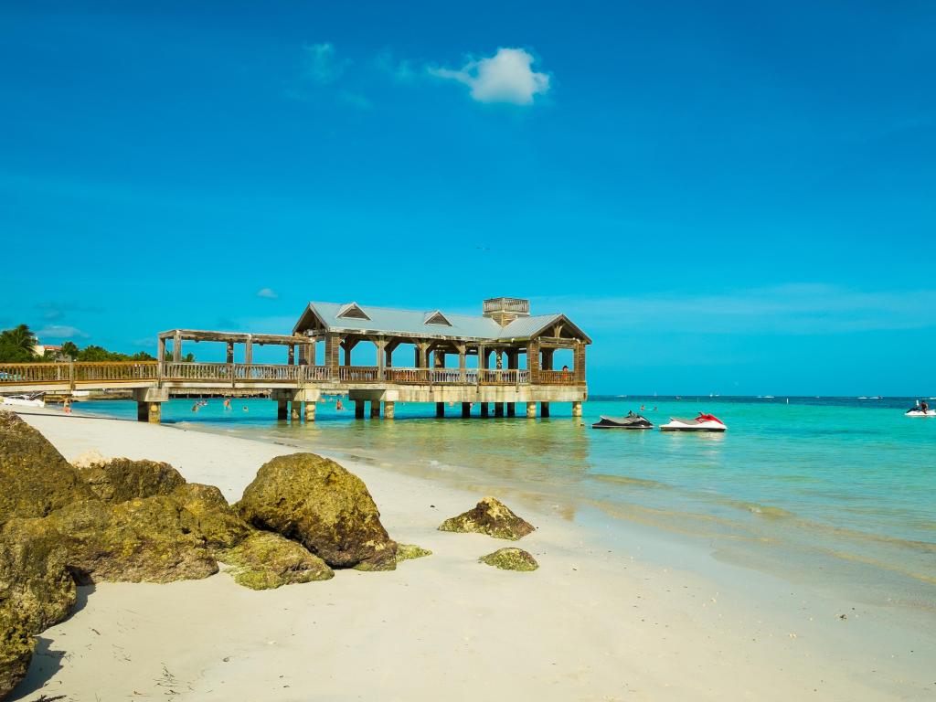 Key West, Florida Keys, USA with a beautiful beach with a  covered pier along the shoreline in the distance and turquoise water.