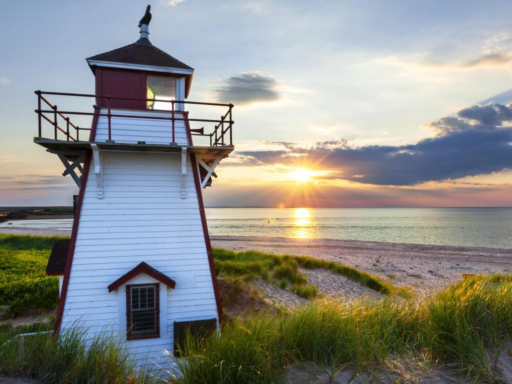 Sunset behind wooden lighthouse right on sandy beach with calm sea