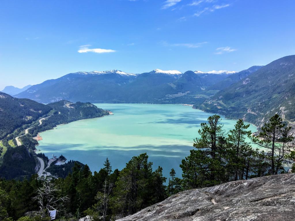 View of turquoise water and snow-capped mountains looking down from a mountain top