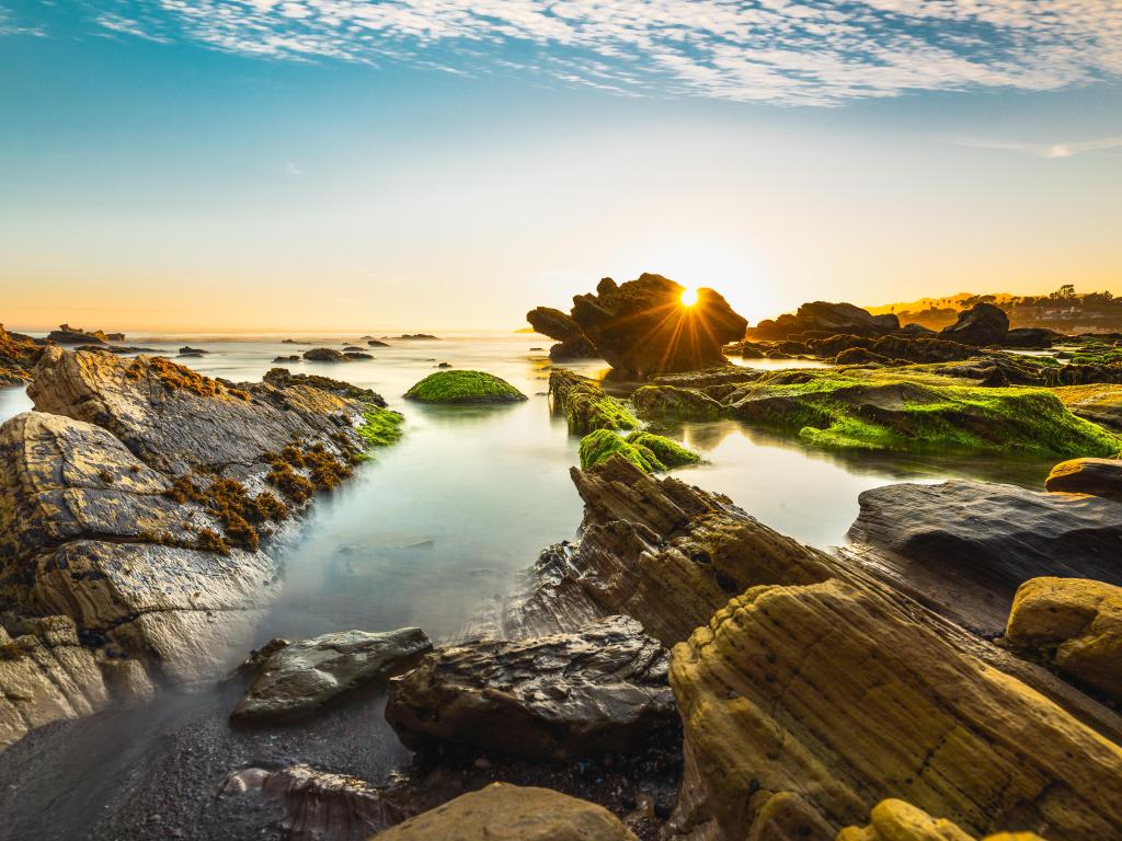 Rocky Riffs at low tide on Pismo Beach, California with sun flare shining through the rocks on the sand