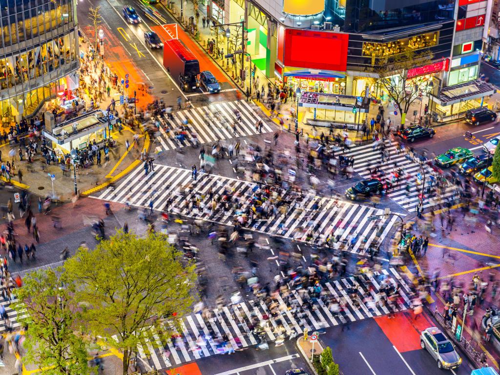 The famously busy Shibuya Crossing in Tokyo at night time, streets are lit by the glowing lights of shops